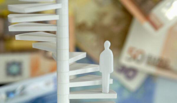 Figur auf Treppe mit Geldscheinen im Hintergrund (Symbolbild) © Westend61 / Achim Sass