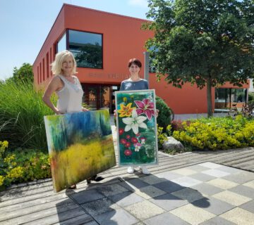 Zwei Frauen präsentieren zwei Gemälde vorm Haus der Familie © Stadt Burghausen