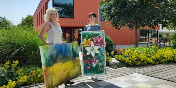 Zwei Frauen präsentieren zwei Gemälde vorm Haus der Familie © Stadt Burghausen