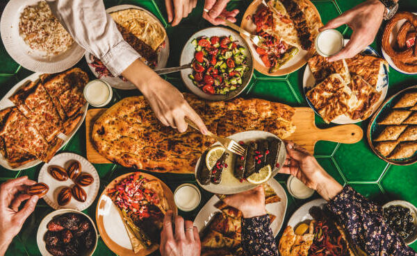 Foto_Fastenbrechen Muslim Ramadan iftar family dinner. Flat-lay of people feasting over table with Middle East food. Dates, dolma, kebab, flatbread, pide, borek, sweet, salad, top view. Ramazan fasting Turkish cuisine
