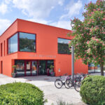 Aussenansicht vom Haus der Familie am Bürgerplatz: Ein Haus mit einer roten Fassade, Fahrräder und Bäume im Vordergrund