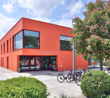Aussenansicht vom Haus der Familie am Bürgerplatz: Ein Haus mit einer roten Fassade, Fahrräder und Bäume im Vordergrund