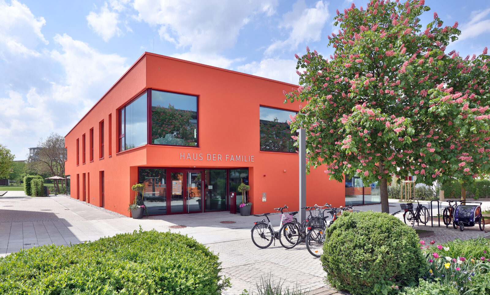 Aussenansicht vom Haus der Familie am Bürgerplatz: Ein Haus mit einer roten Fassade, Fahrräder und Bäume im Vordergrund
