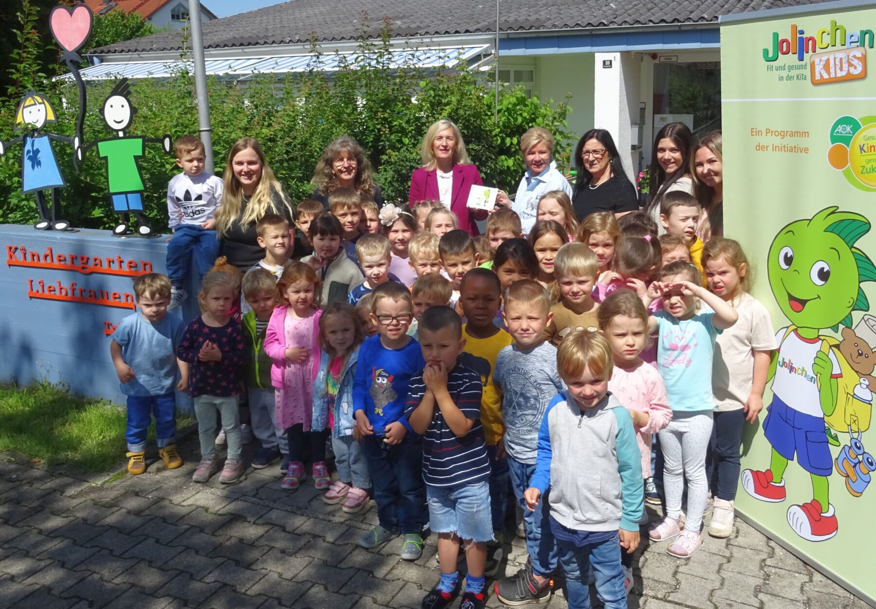 Die Kita Liebfrauen Burghausen ist Jolin-chenKids-Einrichtung. Angela Adelsperger-Birk von der AOK (Mitte.) überreichte das Türschild an Einrichtungsleiterin Esther Wallinger (4.v.re.) und an die Leiterinnen der einzelnen Gruppen mit den Burghausener Kindern