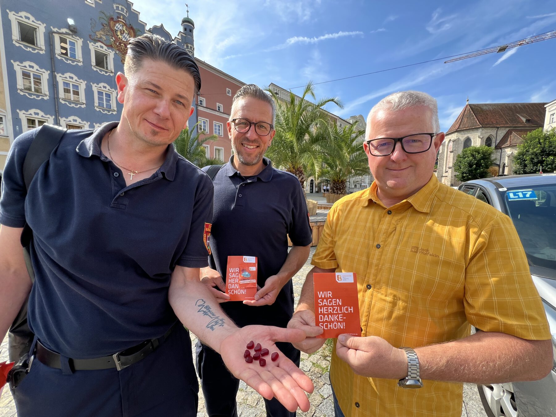 „Ein Herz für Richtigparker“ steht auf den Gummibärchen. „Wir sagen herzlich Dankeschön“ auf der orangen Postkarte. Umseitig erklärt die Stadt Burghausen, was alles richtiggemacht wurde: u.a. keine Geh- oder Radwege blockiert, mit gültiger Parkschreibe geparkt, keine Rettungswege blockiert etc. Verkehrsüberwacher Stefan Wormeck (v.l.), Jens Fichtner und Ordnungsamtsleiter Martin Hinterwinkler zeigen die herzliche Botschaft. Fotocredit: Stadt Burghausen/Königseder