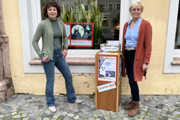 In der Stadtbibliothek ist das Gespenst Toni derzeit nicht zu übersehen. Christin Moll (li.), Leiterin der Stadtbibliothek, und Mitarbeiterin Rosi Pfeifenthaler am Startpunkt des Bilderbuch-Spaziergangs Fotocredit: Stadt Burghausen/sast