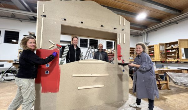 Foto: Die Burghauser Künstlerin Nada Jordan (v.l.), die städtischen Schreiner im Bauhof Markus Salzinger sowie Christoph Bonauer und Sabina Schneider Reisinger beim Streichen der menschlichen Jukebox. Fotocredit: Stadt Burghausen / Königseder