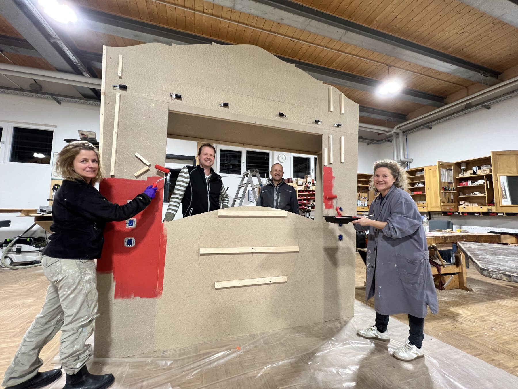 Foto: Die Burghauser Künstlerin Nada Jordan (v.l.), die städtischen Schreiner im Bauhof Markus Salzinger sowie Christoph Bonauer und Sabina Schneider Reisinger beim Streichen der menschlichen Jukebox. Fotocredit: Stadt Burghausen / Königseder