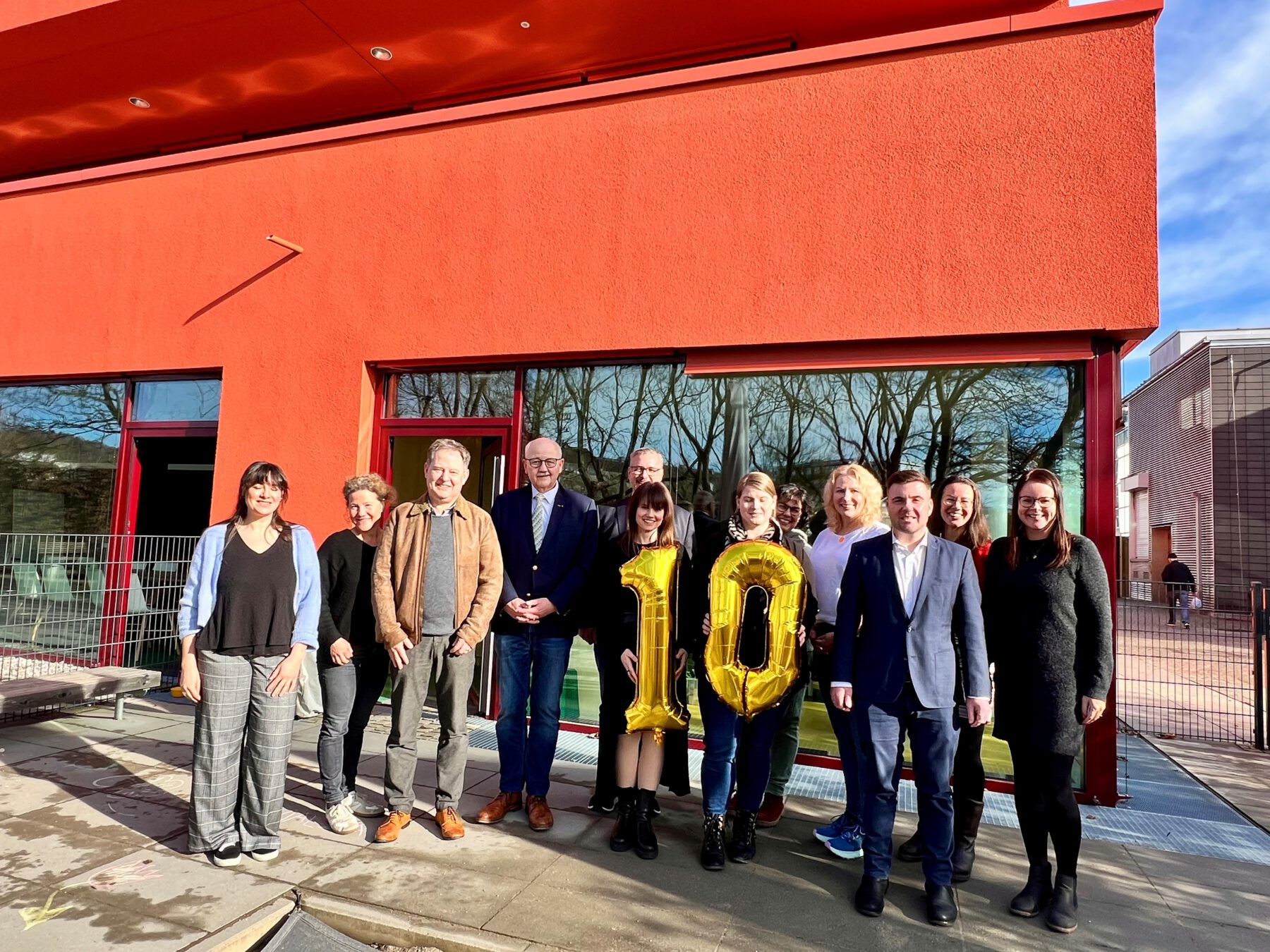 Foto im neuen Außenbereich der Kita Kunterbunt mit altem und neuen Träger (v.l.): Haben eine 10 mitgebracht, weil die Burghauser Kita Kunterbunt die 10. Kita in der Trägerschaft des BRK Kreisverbands ist. Mariella Röben, Leitung der Geschäftsstelle, Sabina Schneider-Reisinger, Vorstand Kinderschutzbund Burghausen-Altötting, Erster Bürgermeister Florian Schneider, Herbert Hofauer, Vorsitzender des BRK-Kreuzverbandes Altötting, Sabine Meier und Martina Klinger vom BRK, Verena Novak und Conny Reichert von der Kita Kunterbunt, Max Gschwendtner Leitung BRK Kinder- Jugendbereich, Christine Auberger, Leitung Haus der Familie und Daniela Spiegelhauer von der städtischen Kämmerei zuständig für die Burghauser Kitas. Fotocredit: Stadt Burghausen / Königseder