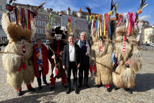 Foto: Im Kreise wilder Kerle: Elisabeth Hübner (2 v.l.), Referentin des Burghauser Partnerstadtvereins für Ptuj, Erster Bürgermeister Florian Schneider und Zweiter Bürgermeister Norbert Stranzinger (Mitte), umringt von einigen Ptujer Kurenten mit ihren farbenprächtigen Masken und mächtigen Knüppeln. Fotocredit: Stadt Burghausen/sast