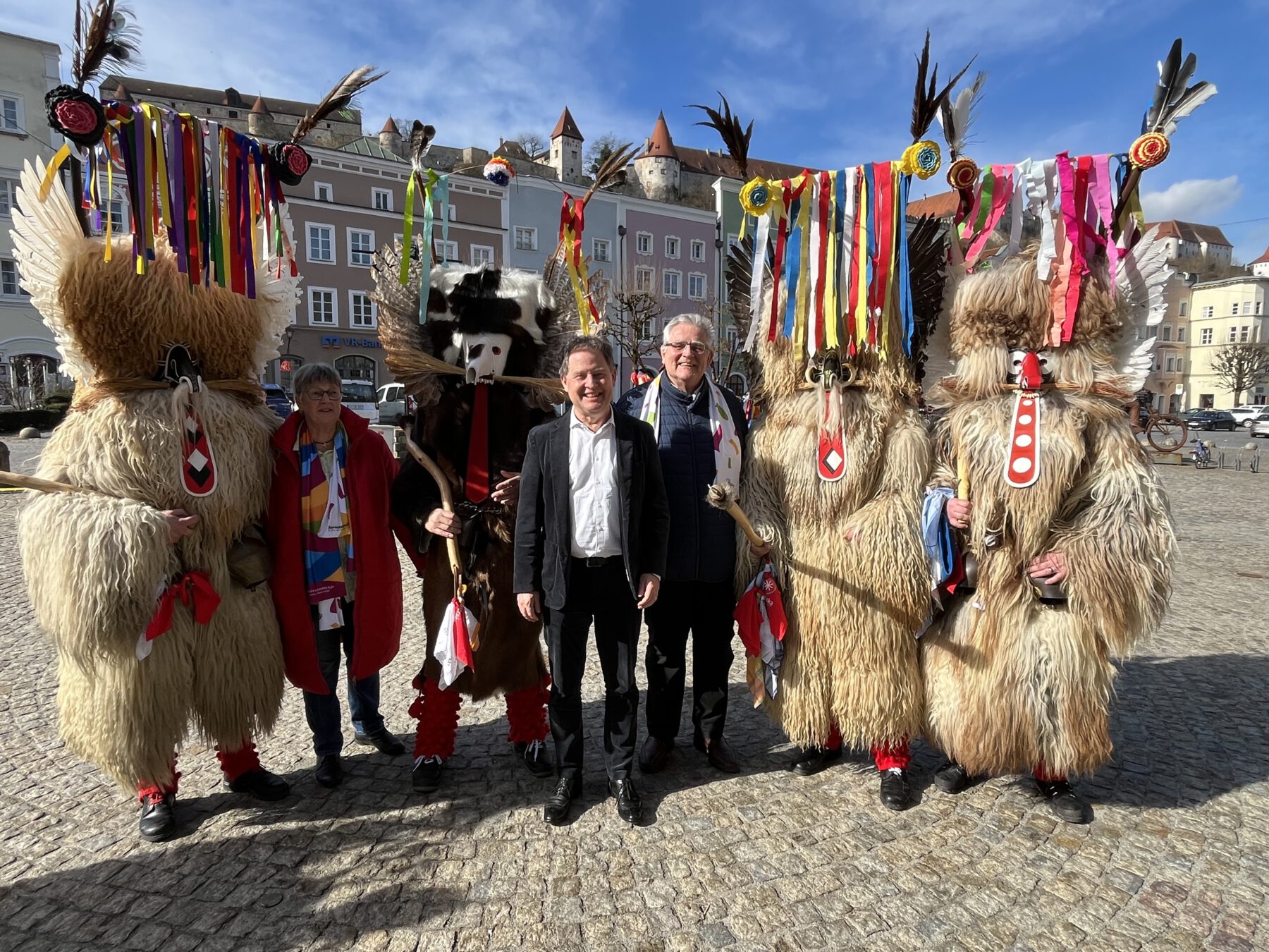 Foto: Im Kreise wilder Kerle: Elisabeth Hübner (2 v.l.), Referentin des Burghauser Partnerstadtvereins für Ptuj, Erster Bürgermeister Florian Schneider und Zweiter Bürgermeister Norbert Stranzinger (Mitte), umringt von einigen Ptujer Kurenten mit ihren farbenprächtigen Masken und mächtigen Knüppeln. Fotocredit: Stadt Burghausen/sast