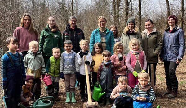 Die Kinder des Montessori Waldkindergarten Burghausen mit FÖJlerin Annalena Wallner (nicht im Bild Joel Feige), den Betreuerinnen und Erzieherinnen vom Waldkindergarten, der Naturschutzbeauftragten Susanne Unterstaller und Ines Huber vom städtischen Umweltamt. Vorne links ist eine frisch gepflanzte Elsbeere zu sehen, die die Kinder auch sofort noch gegossen haben. Fotocredit: Stadt Burghausen / köx