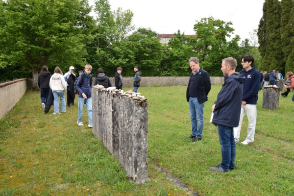 FOTO: In Gedenken an 80 Jahre Kriegsende: 1. Bürgermeister Florian Schneider und Stefan Angstl, 3. Bürgermeister und Lehrer am AVG, betrachten Grabsteine auf dem KZ-Friedhof am Pulverturm, während Schülerinnen und Schüler symbolisch nach jüdischer Sitte Steine ablegen. Fotocredit: Stadt Burghausen / Gauer