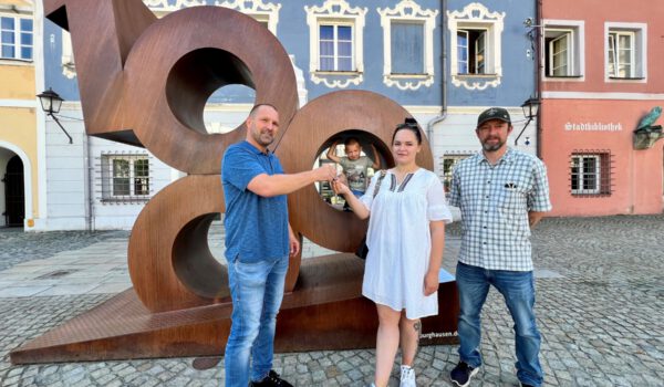 Erfolg durch gute Zusammenarbeit: Wohnungsschlüssel-Übergabe an WOHIN-Projektteilnehmerin Olena Nechvolod (mit Sohn Matvii) durch Herrn Michael Madl (l.), Gebäudemanager der Stadt Burghausen, mit Markus Huber, BRK-Projektleiter (r.). Fotocredit: Stadt Burghausen / köx