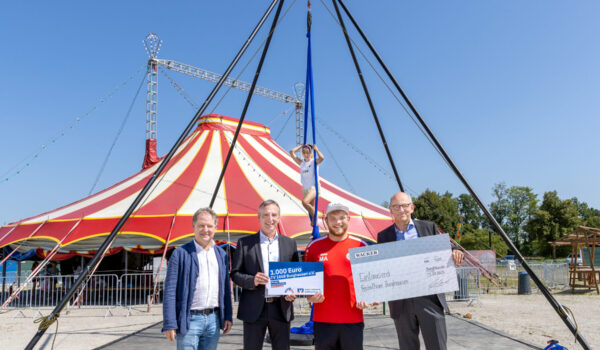 Bei der Spendenscheckübergabe (v. l.): 1. Bürgermeister Florian Schneider, Marktdirektor der VR-Bank im Bereich Burghausen Robert Oberreiter, Leiter Freizeitheim und der Abteilung Zirkus beim TV 1868 Marcel Anslinger sowie WACKER-Werkleiter Peter von Zumbusch. Im Hintergrund Carolina Zellbeck im Luftgestell. (Quelle: Wacker Chemie AG)