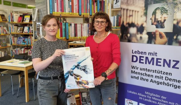 Veronika Alfranseder, Leiterin Seniorenbüro und Quartiersmanagerin der Stadt Burghausen und Christin Moll, Leiterin der Stadtbibliothek Burghausen präsentieren das Plakat zur 6. Bayerischen Demenzwoche, an der sich auch Burghausen mit einem eigenen Programm beteiligt. Fotocredit: Stadt Burghausen / köx