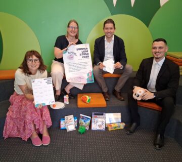 Foto: Vier Stempel einsammeln und – Bingo! So funktioniert der Sommerlesespaß in der Stadtbibliothek  Das Team der Stadtbibliothek mit Leiterin Christin Moll und Mitarbeiterin Monika Vornehm ist bereit für den Kinderansturm, Sebastian Rauschecker und David Gergely Komaromi von der Sparkasse Burghausen sponserten dieses Mal die Sofortgewinne  Fotocredit: Stadt Burghausen/tg