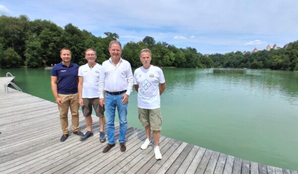 2026_07_22_Stadt_Burghausen_Freiwassermeisterschaften_Wöhrsee Sie rechnen mit besten Wettkampfbedingungen am kommenden Samstag am Wöhrsee: (v.l.): Stefan Sajdak, Burghauser Bäderleiter, Volker Mucks, Abteilungsleiter Schwimmen beim SV Wacker Burghausen, Erster Bürgermeister Florian Schneider sowie Stefan Hetzer, Sportlicher Leiter SVW Schwimmen. Fotocredit: Stadt Burghausen/tg