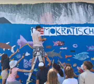 Farbenrausch in der Unterwasserwelt: Graffiti Künstler Martin Keindl leitete die Kinder bei der Umsetzung ihrer kreativen Ideen an, die Kinder reichten ihm die Spraydosen für den Schriftzug  Fotocredit: Stadt Burghausen/tg