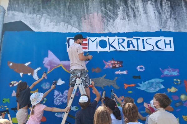 Farbenrausch in der Unterwasserwelt: Graffiti-Künstler Martin Keindl leitete die Kinder bei der Umsetzung ihrer kreativen Ideen an, die Kinder reichten ihm die Spraydosen für den Schriftzug. Fotocredit: Stadt Burghausen/tg