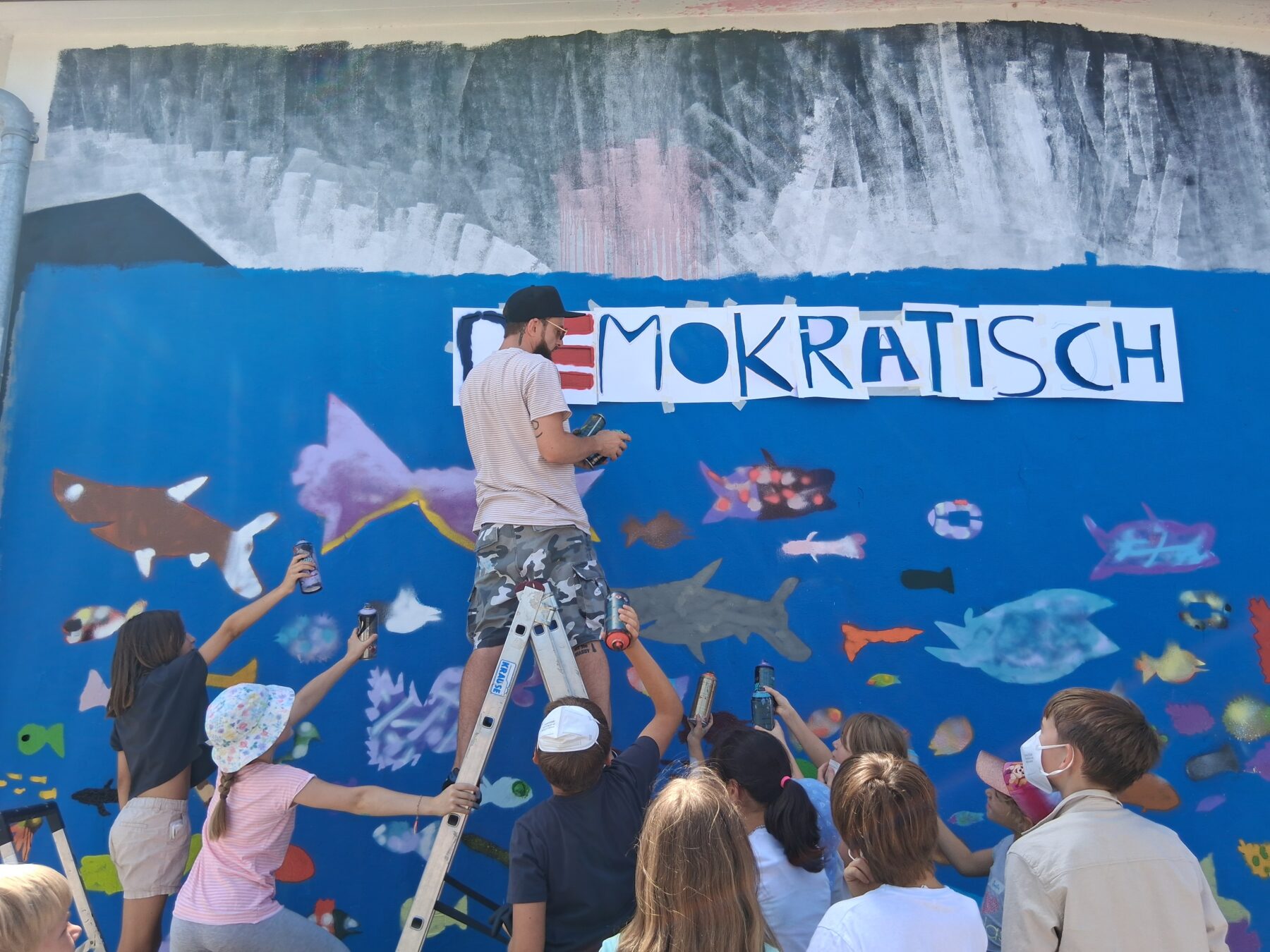 Farbenrausch in der Unterwasserwelt: Graffiti Künstler Martin Keindl leitete die Kinder bei der Umsetzung ihrer kreativen Ideen an, die Kinder reichten ihm die Spraydosen für den Schriftzug Fotocredit: Stadt Burghausen/tg