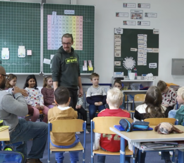Szene aus dem neuen Film „Starke Jugend“, zu sehen auf dem YouTube Kanal der Stadt Burghausen: Martin Höllmüller (stehend) und Germain Bennett (l ) spielen mit den Schülerinnen und Schülern echte Situationen aus ihrem (Schul )Alltag durch  Fotocredit: Stadt Burghausen