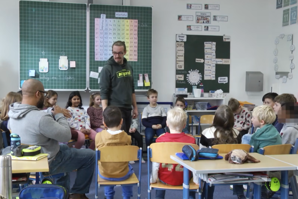 Szene aus dem neuen Film „Starke Jugend“, zu sehen auf dem YouTube Kanal der Stadt Burghausen: Martin Höllmüller (stehend) und Germain Bennett (l.) spielen mit den Schülerinnen und Schülern echte Situationen aus ihrem (Schul-)Alltag durch. Fotocredit: Stadt Burghausen