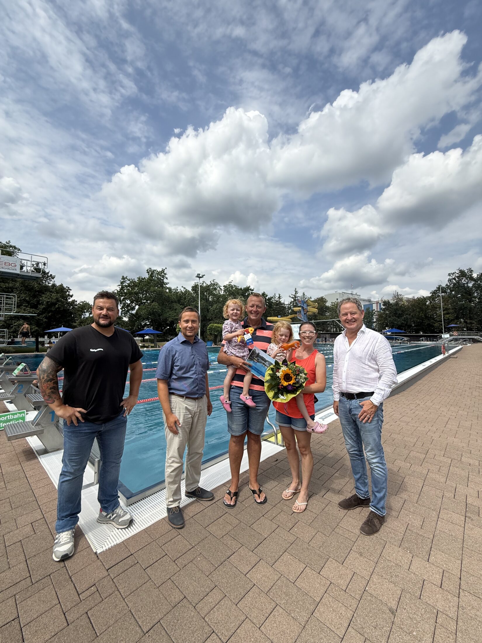 Erster Bürgermeister Florian Schneider begrüßte gemeinsam mit Bäderleiter Stefan Sajdak und Florian Moser die Familie Kornberger aus Ampfing als 100 000 Badegäste der Freibadsaison 2026 im Burghauser Freibad Zur Überraschung gab es Blumen für Susanne Kornberger, Taucherbrillen für Teresa und Valentina sowie eine Saisonkarte 2027 für die ganze Familie Fotocredit: Stadt Burghausen / köx